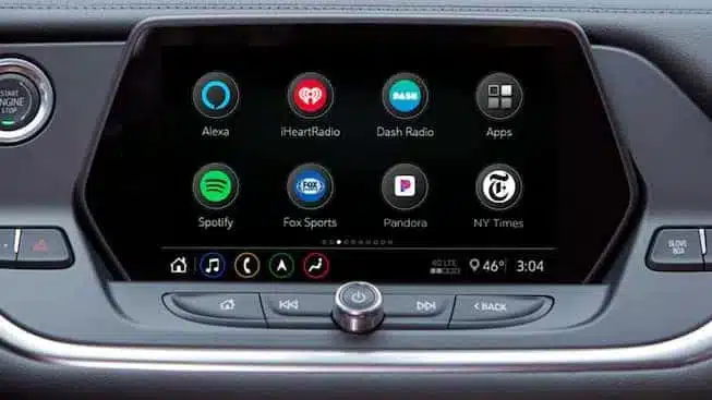 Car infotainment system display featuring apps like Spotify, Pandora, iHeartRadio, and Fox Sports, along with controls for voice assistance and connectivity options. The screen shows the temperature at 46°F and the time as 3:04.