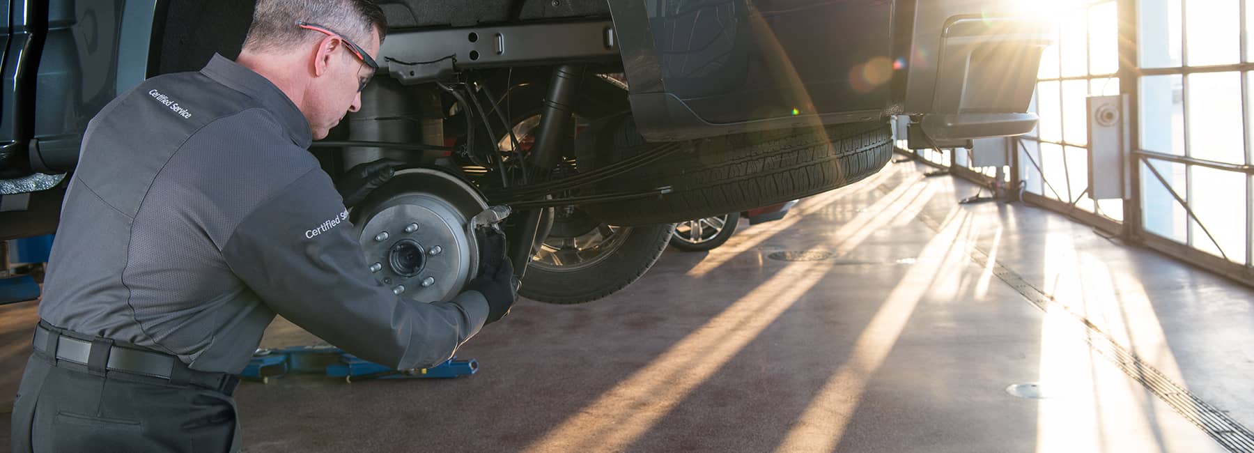 A mechanic servicing the brake system of a truck in a well-lit auto repair shop, demonstrating professional vehicle maintenance with tools in hand.