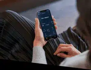A close-up of a person's hand holding a smartphone displaying a modern mobile app interface, with sleek design elements, on a cozy setting featuring a soft gray sweater and a striped skirt.