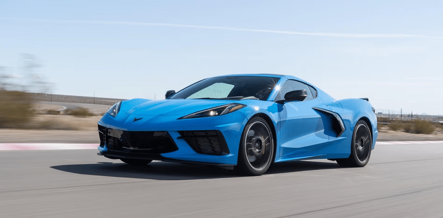 Blue Chevrolet Corvette C8 speeding on a winding racetrack under a clear blue sky, showcasing its sleek design and sporty profile.