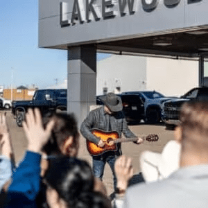 Musician performing outdoors in front of Lakewood dealership, entertaining a crowd with an acoustic guitar under clear skies.