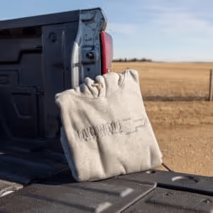 Gray hoodie with a logo hanging on the edge of a truck bed in an open field under a clear sky.