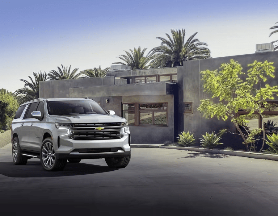 Silver Chevrolet SUV parked in front of a modern architectural home surrounded by palm trees and greenery. The image showcases the vehicle's sleek design and contemporary setting, emphasizing luxury and outdoor living.