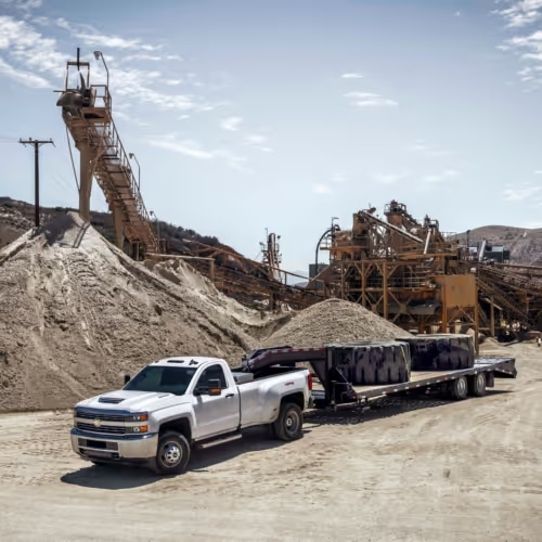 Heavy-duty truck transporting materials in a construction site with machinery and sand piles in the background, showcasing industrial operations and logistics.
