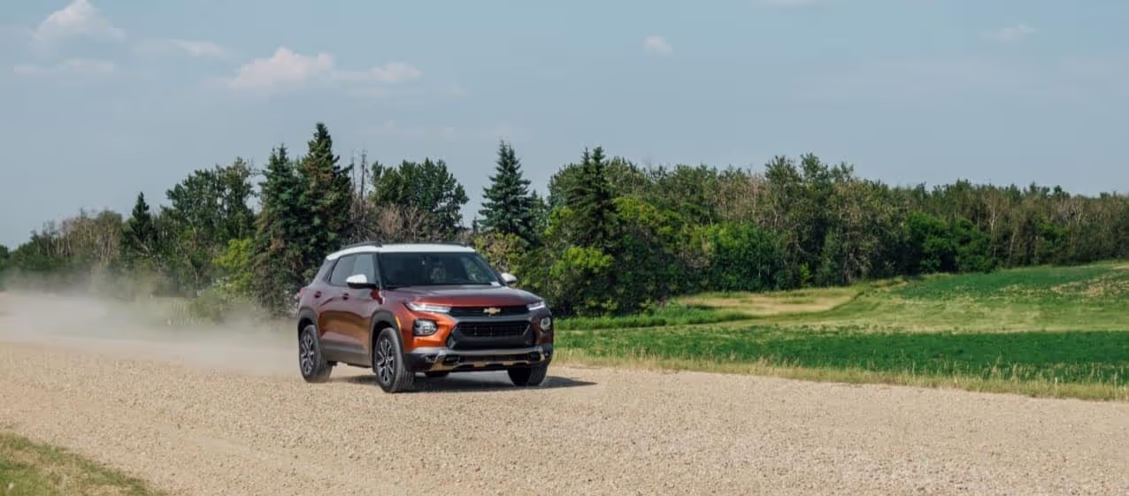 A Chevrolet SUV driving on a gravel road surrounded by lush greenery and trees under a clear blue sky, showcasing its off-road capabilities and exterior design.