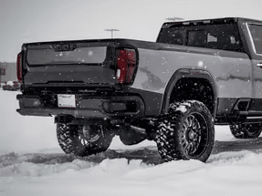 Gray pickup truck with oversized tires parked in snowy conditions, showcasing its off-road capabilities and rugged design.