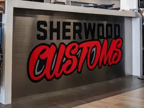 Signage displaying the logo of Sherwood Customs, featuring bold red lettering on a metallic background, located in a modern retail space.