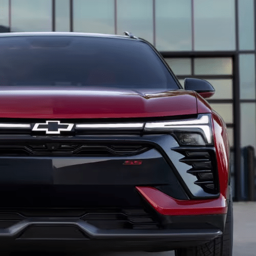 Close-up front view of a red Chevrolet SS SUV showcasing its sleek design and modern headlights against a contemporary glass building background.