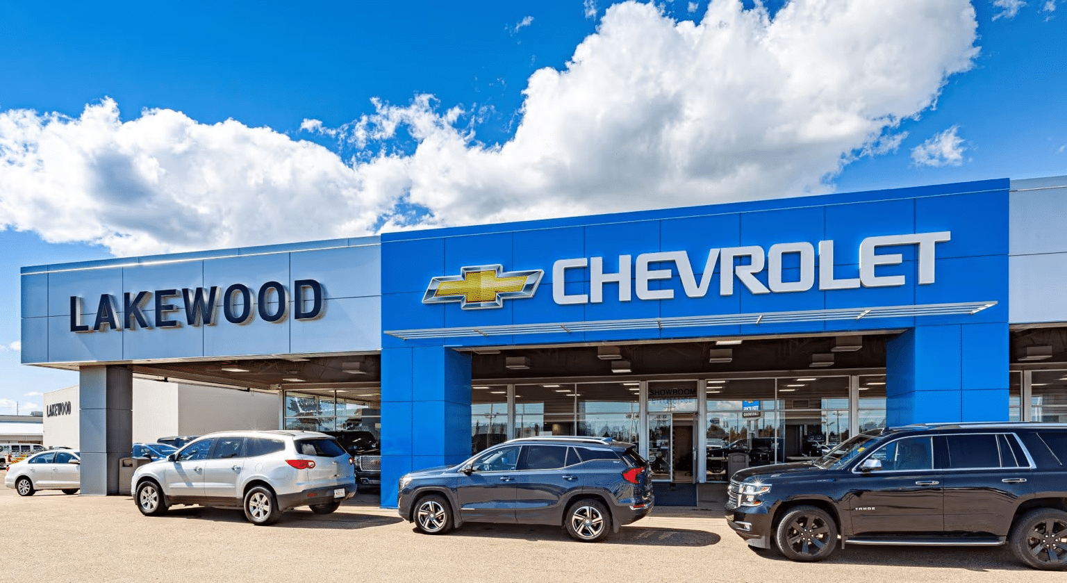 Chevrolet dealership sign in Kelowna, featuring a large blue logo and colorful banners overhead against a cloudy sky.